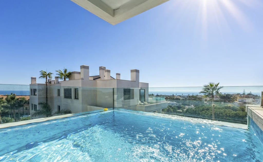 Rooftop infinity pool with glass balustrade overlooking sea and palm trees at a Spanish coastal property