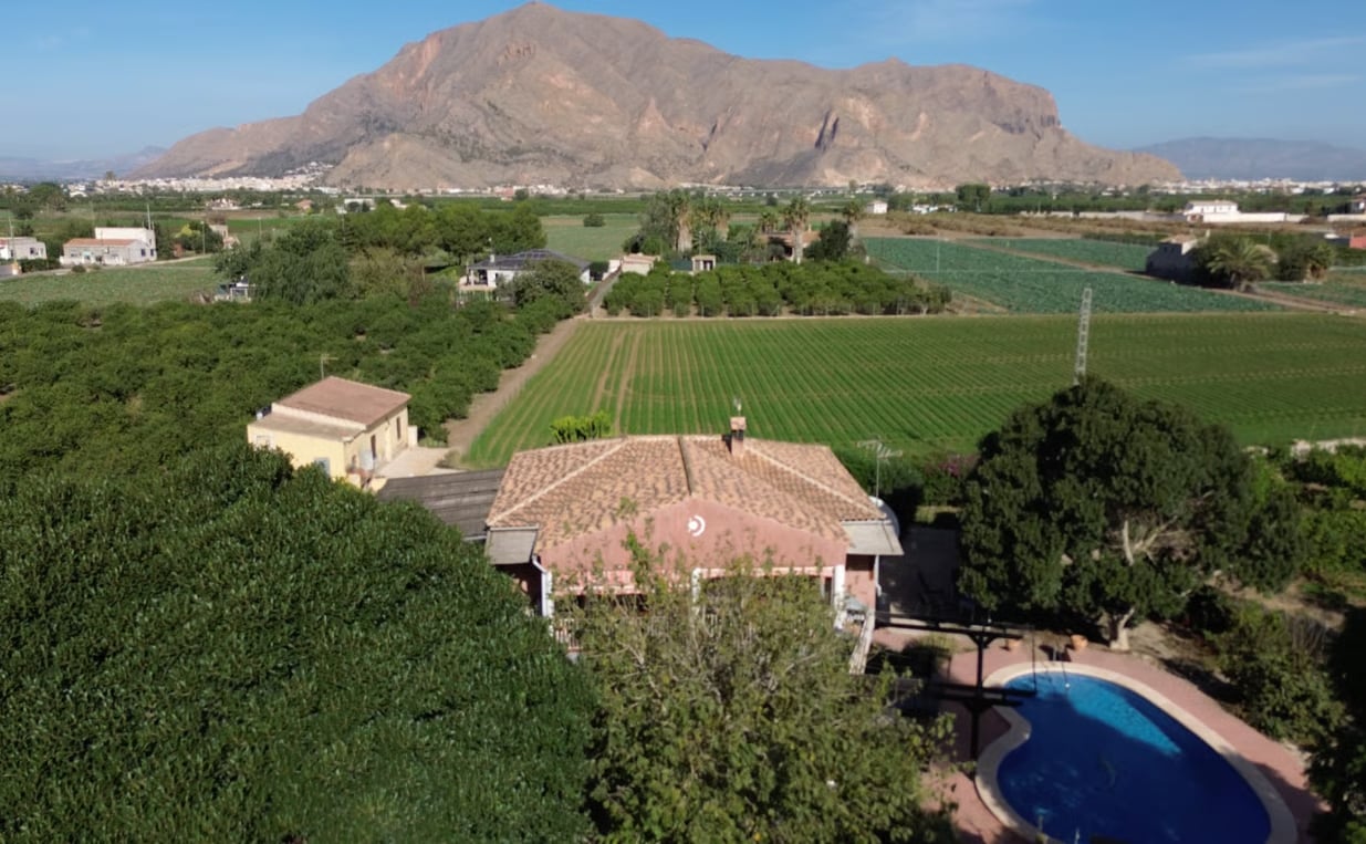 Terracotta-roofed Spanish villa with kidney-shaped pool surrounded by orchards and mountain scenery