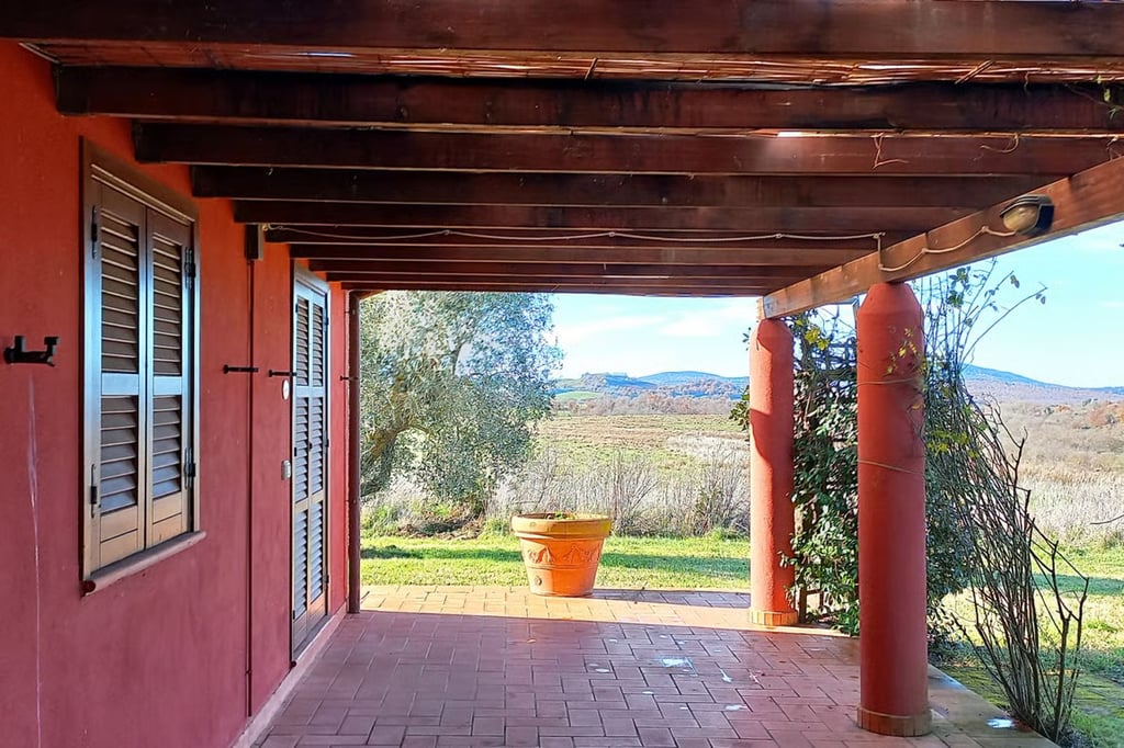 Covered terrace at a Capalbio property, with terracotta walls, wooden beams, tiled flooring and views over open fields.
