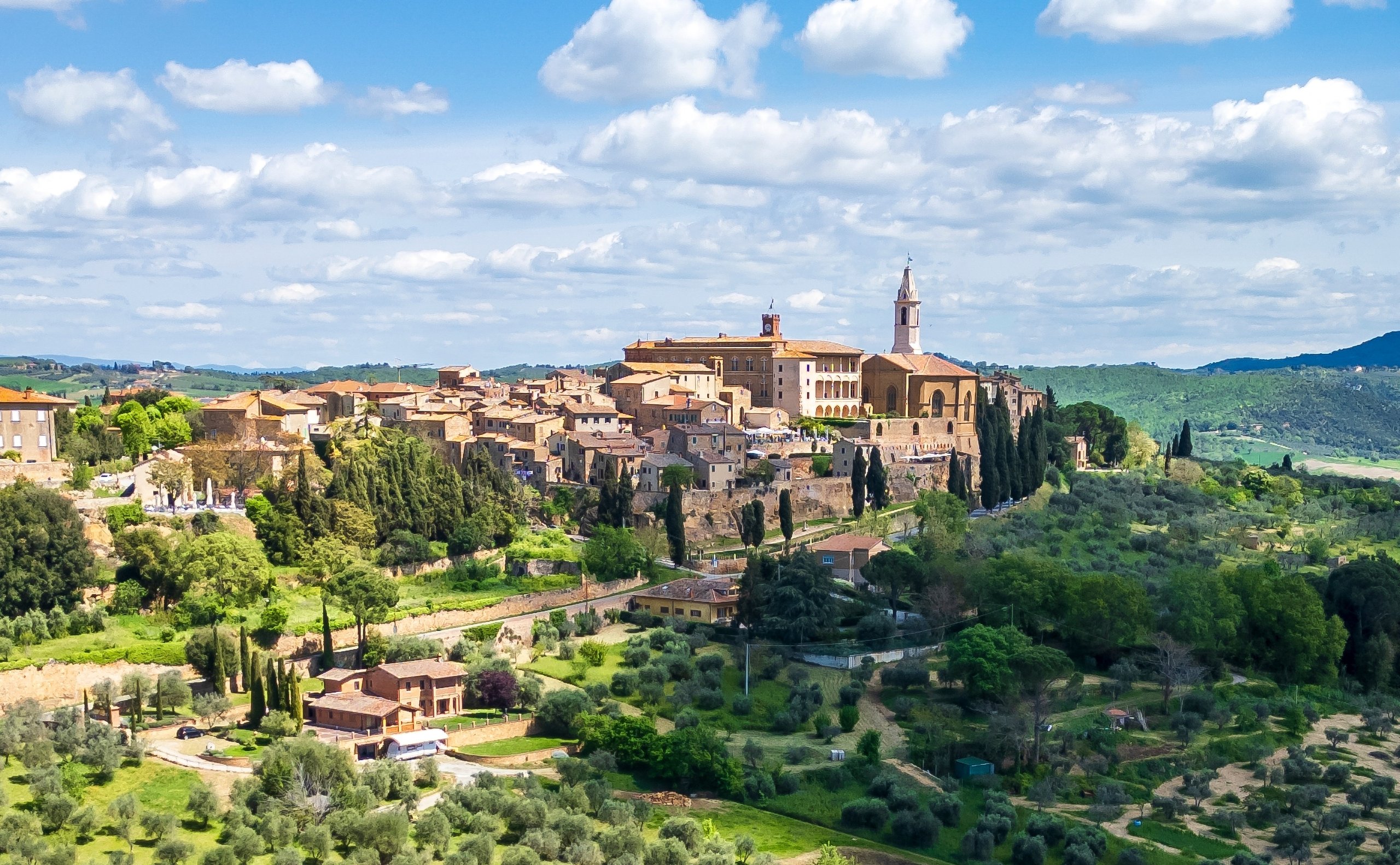 Historic hilltop town of Pienza in Tuscany, with its cathedral bell tower, terracotta rooftops, olive groves and green hills.