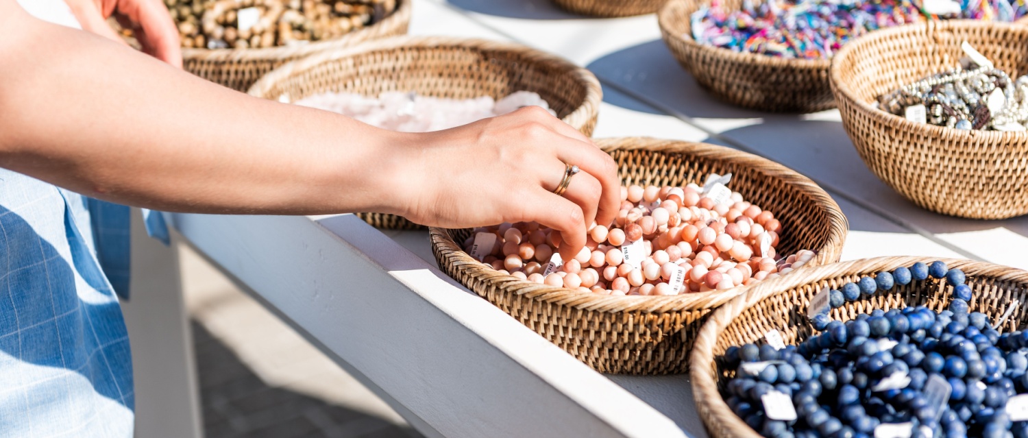 Closeup of young woman shopping for colorful stone beach bracelets touching hand in outdoor market shop