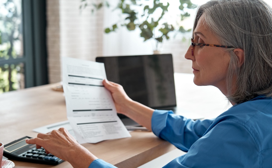 Senior mature business woman holding paper bill using calculator old lady managing account finances
