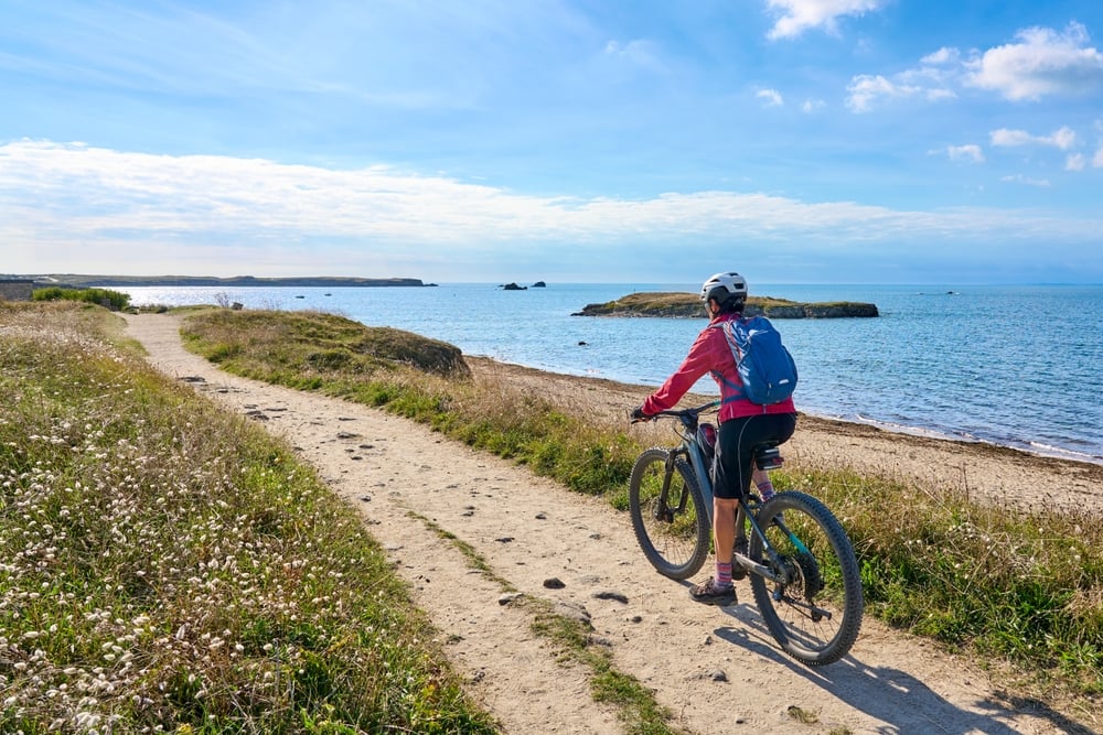 active senior woman cycling with her electric mountain bike at the wild coast of Quiberon peninsula, Brittany, France