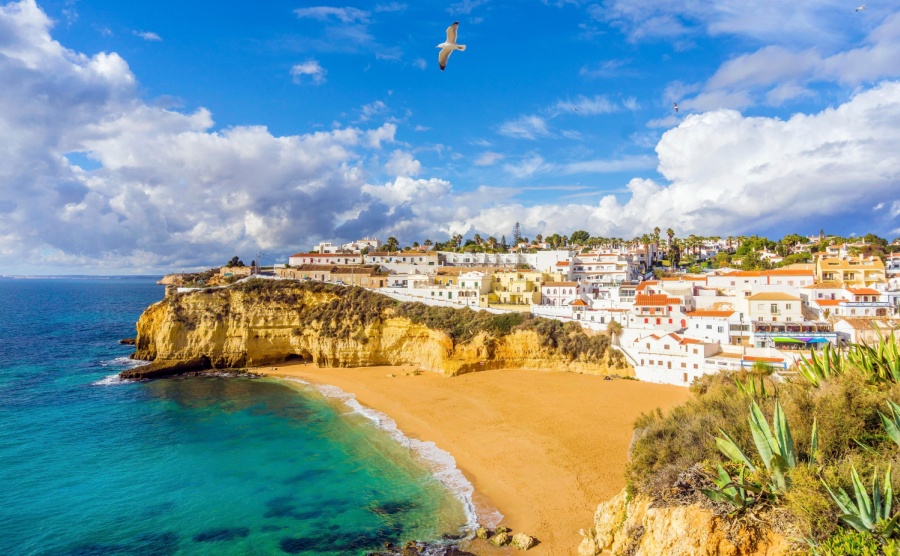 Wide sandy beach, white houses cloudy sky with seagulls Carvoeiro Algarve Portugal