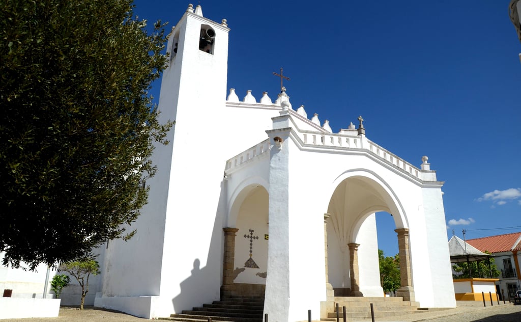 Affordable property area in the Alentejo, Portugal, with a whitewashed church, bell tower and arched portico under blue sky.