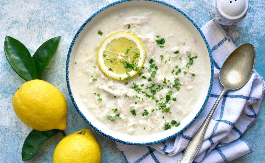 Avgolemono - traditional greek chicken soup with orzo pasta, eggs and lemon in a vintage bowl over light blue slate, stone or concrete background.