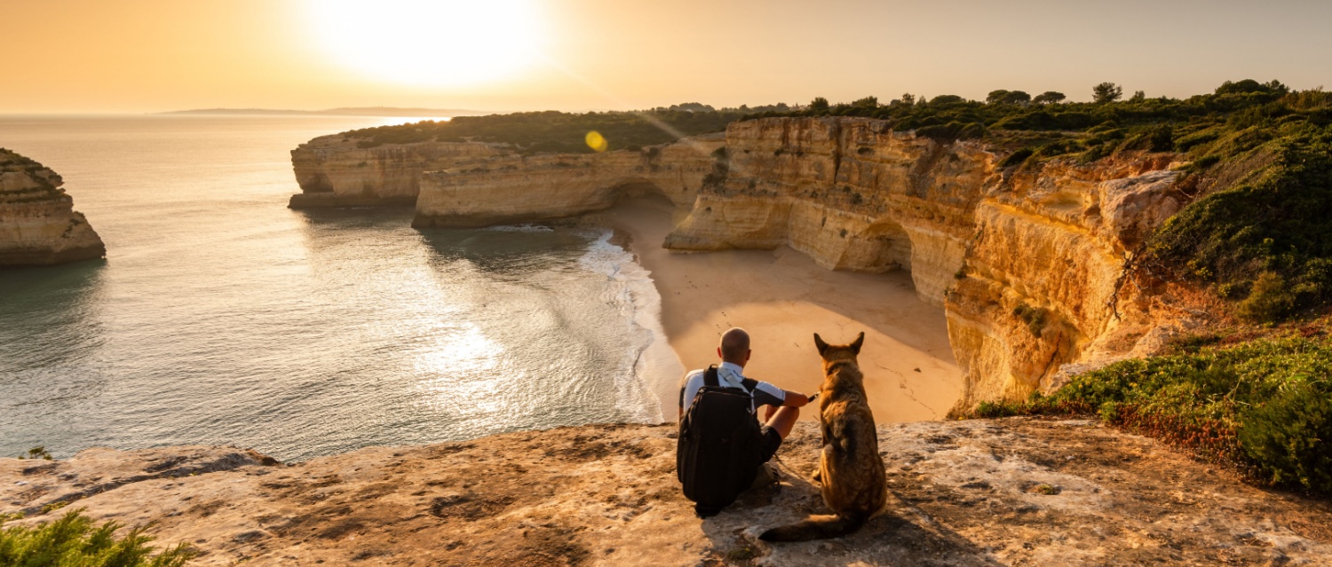 Friendship and Togetherness Concept. Man and Dog Looking at Sunset at Sea Cliffs in Portugal.