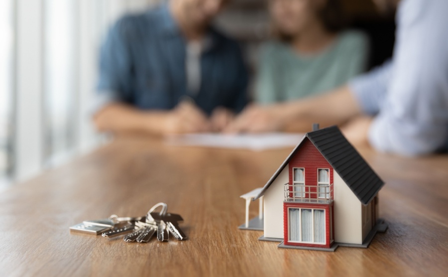 Close up of key and tiny toy house on table. Married couple buying house, consulting, lawyer, legal advisor, real estate agent, bank manager, signing mortgage agreement in background