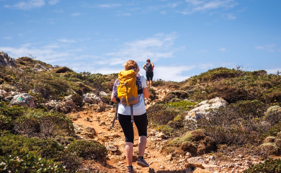 Two female hikers with backpack walking up to cliffs on Algarve coastline in Portugal. Active summer hiking vacation