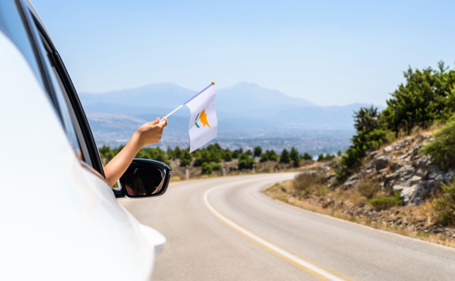 Woman holding Cyprus flag from the open car window driving along the serpentine road in the mountains.