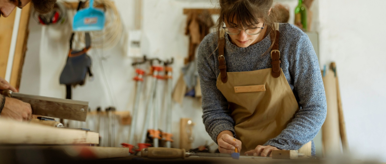 A young female carpenter working as wood designer in a small carpentry workshop. Young business woman handcrafting a piece of timber and designing new house furniture. Entrepreneurs concept lifestyle