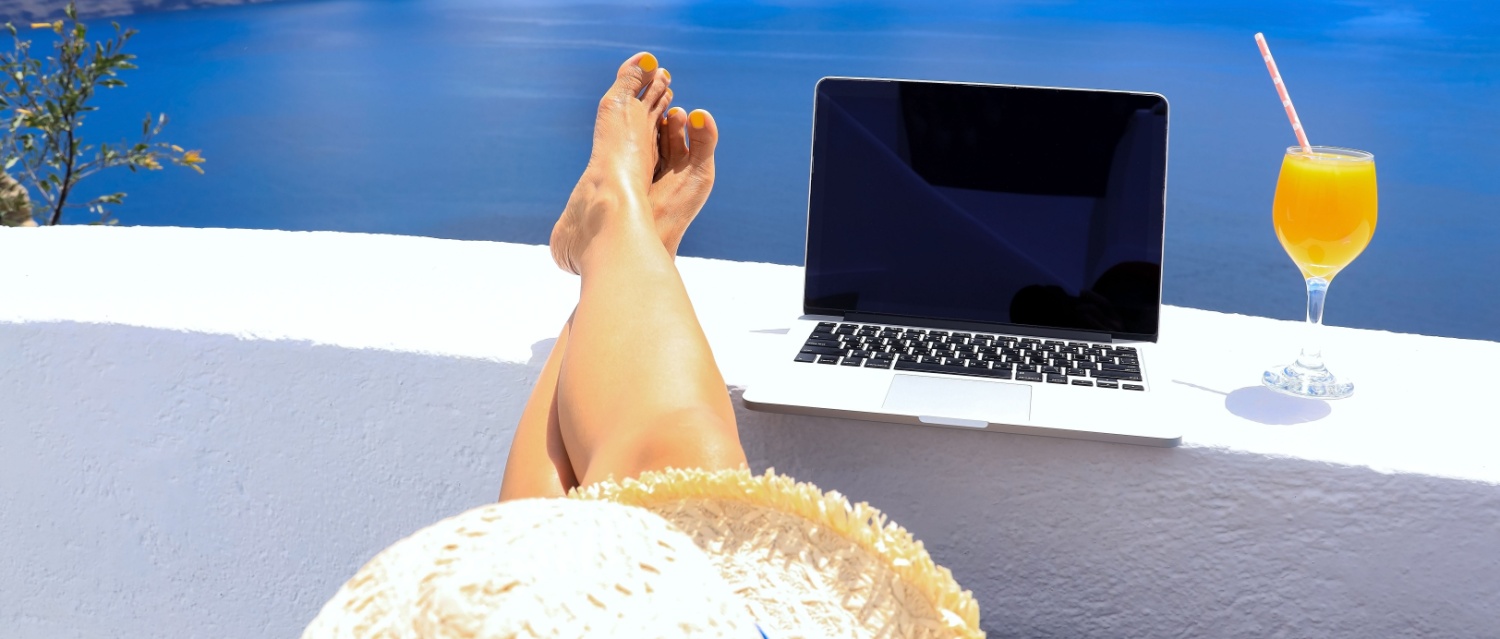 Woman with her feet up next to a laptop, working in the sun with a cocktail