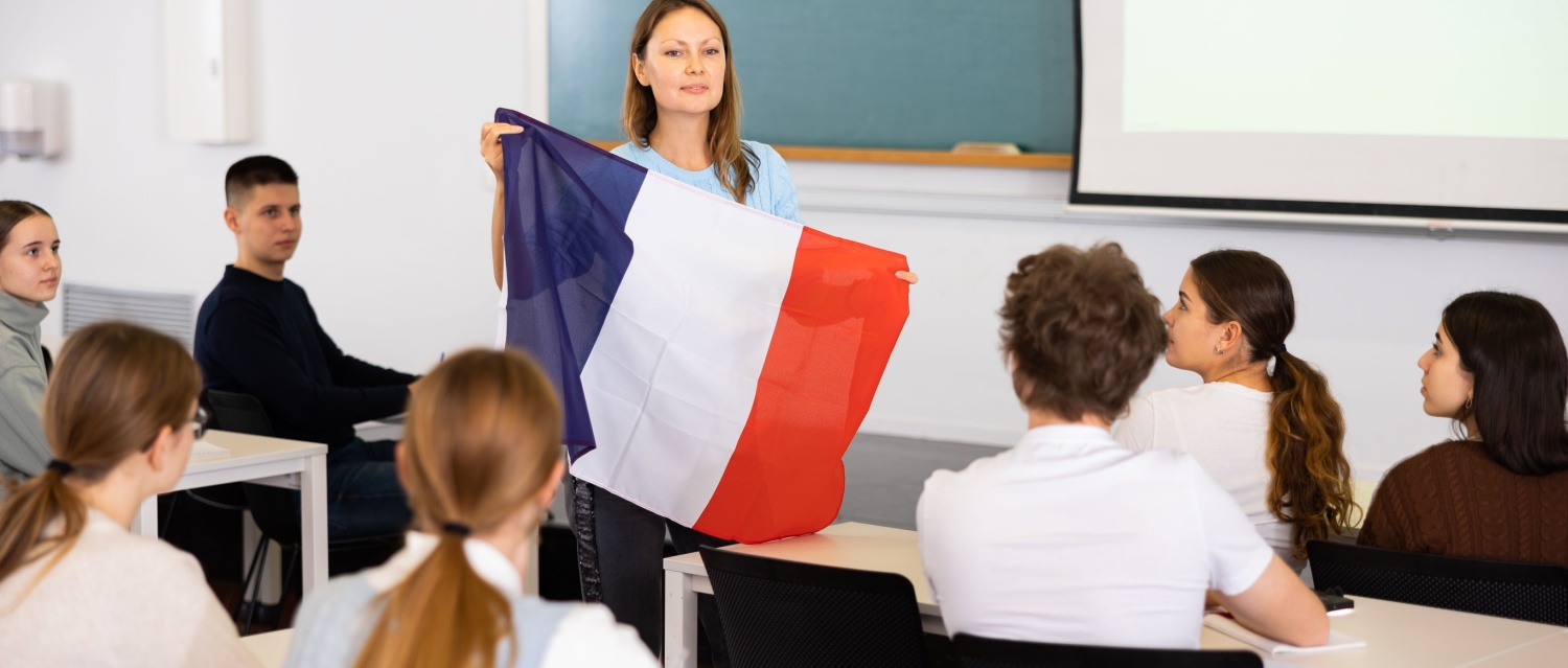 Geography lesson in school class - teacher talks about France, holding a flag in her hands
