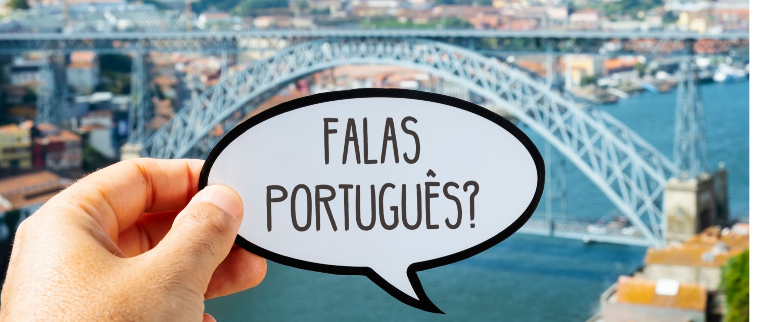 the hand of a man holding a speech bubble with the question falas portugues, do you speak Portuguese? written in Portuguese, in Porto, Portugal, with the famous Dom Luis I Bridge in the background