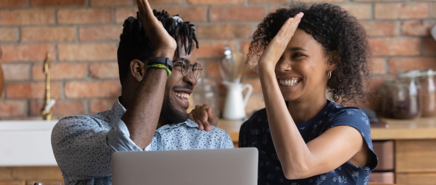 Happy excited Black multiracial couple celebrating financial success at laptop getting income loan mortgage bank approval planning good family budget. Young husband and wife giving high five