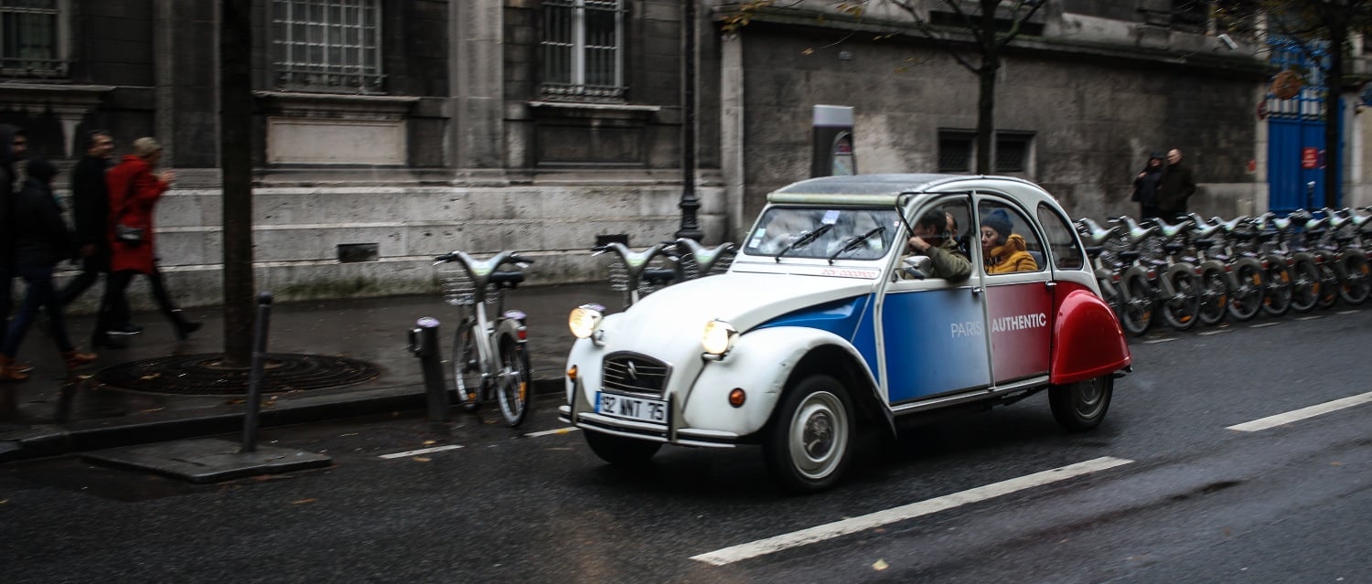 A modern car driving through a quiet French village, illustrating owning a car in France