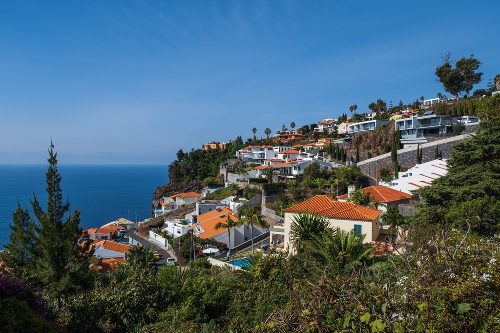 White-walled villas with terracotta roofs on a green hillside overlooking the Atlantic Ocean in Madeira, Portugal