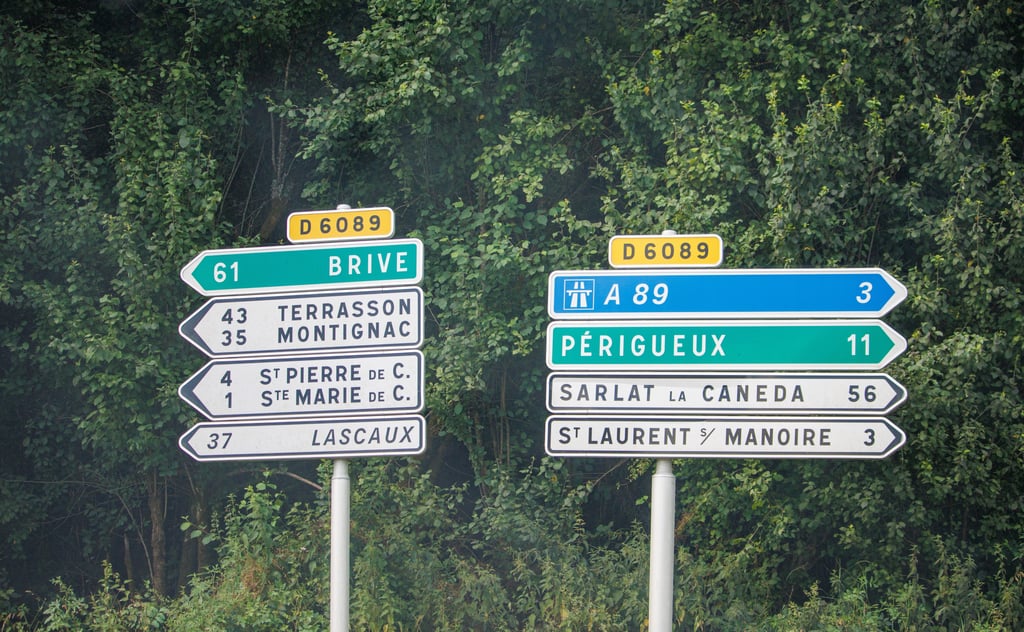 A yellow diamond road sign with a black diagonal line next to an 'X' in a triangle sign on a quiet French country road.