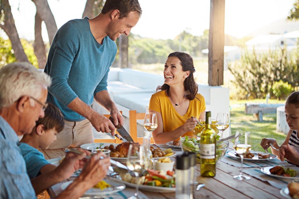 Three generations of a family share an outdoor meal on a sunny terrace with wine and fresh food