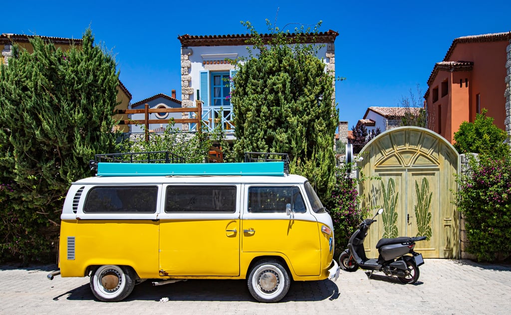 Yellow camper van with roof rack parked outside a Mediterranean-style house with blue shutters