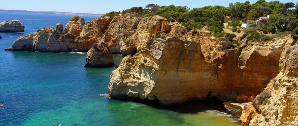Rocky golden cliffs and turquoise sea along the Algarve coastline in Portugal on a sunny day