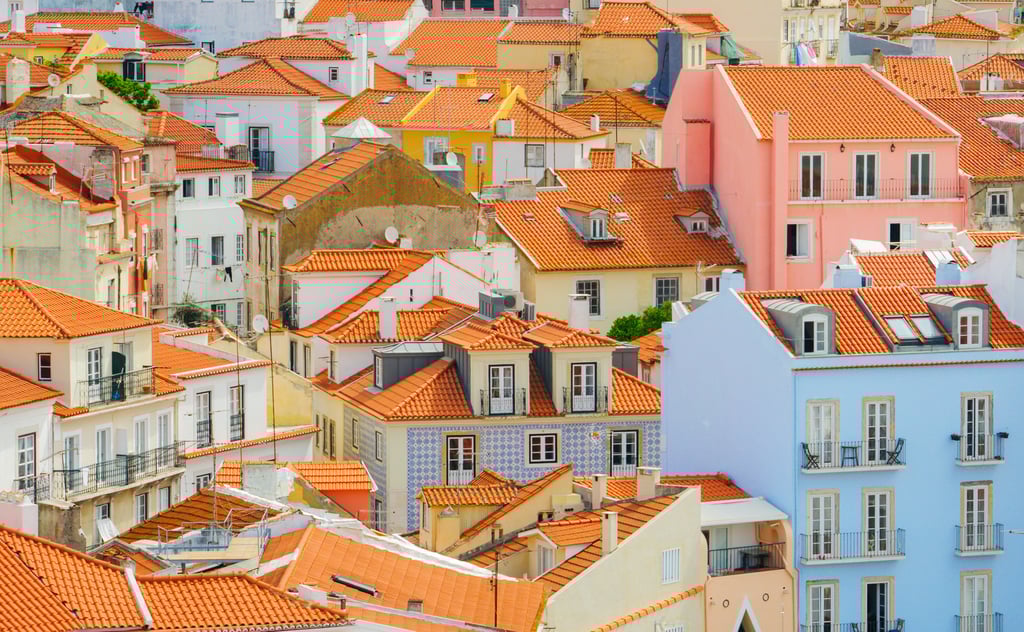 Terracotta tiled rooftops of traditional houses in Lisbon, Portugal, with the city skyline in the background