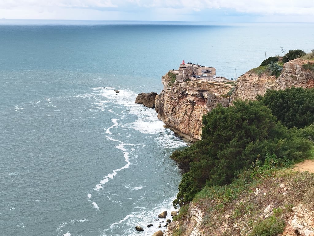 Silver Coast Portugal cliff and lighthouse above Atlantic waves near Nazaré for Algarve vs Silver Coast comparison.