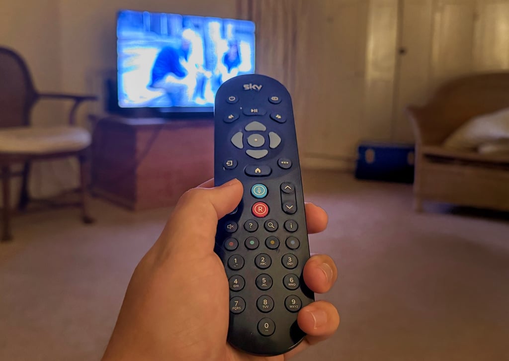 Hand pointing Sky remote control at TV