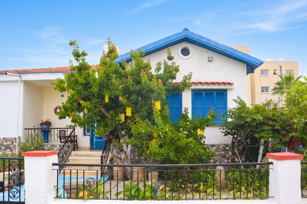 Traditional Cypriot house with blue shutters, red-tiled roof and pebble-stone garden wall