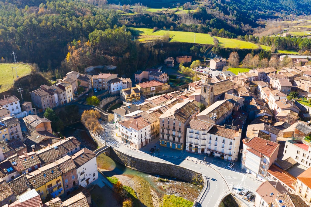 Aerial view of La Pobla de Lillet, a small Spanish town with terracotta rooftops beside a curving road