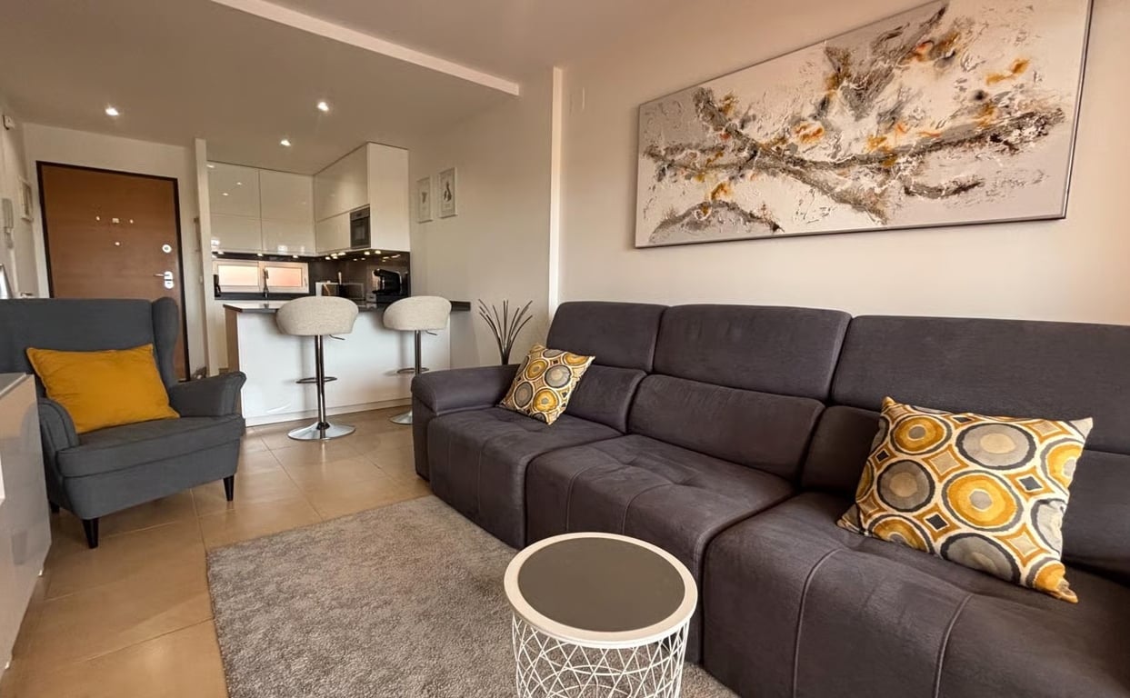 Grey sofa with mustard cushions sits beside an open-plan kitchen in this overseas property