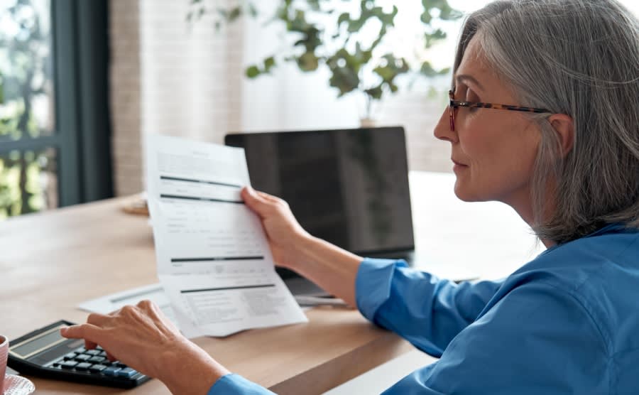 Senior mature business woman holding paper bill using calculator old lady managing account finances