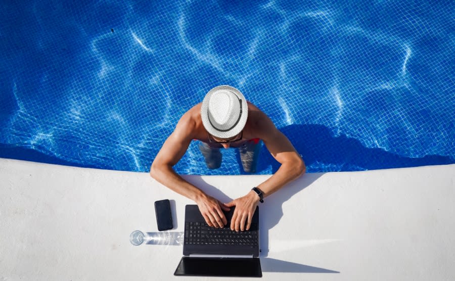 A digital nomad works in the pool, typing on their laptop, enjoying the sun