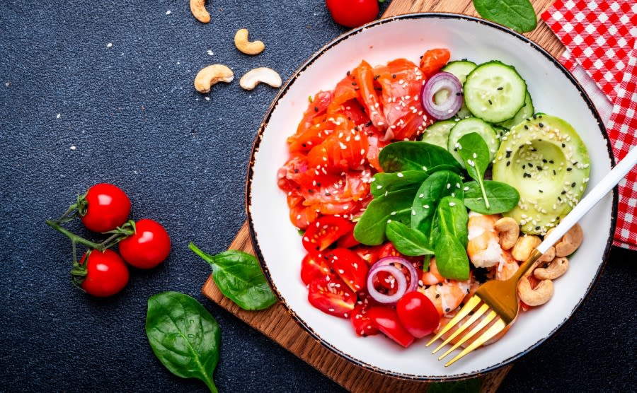 Seafood salad bowl with salmon, shrimp, avocado, spinach, cucumber, tomato, cashew and sesame. Black background, top view