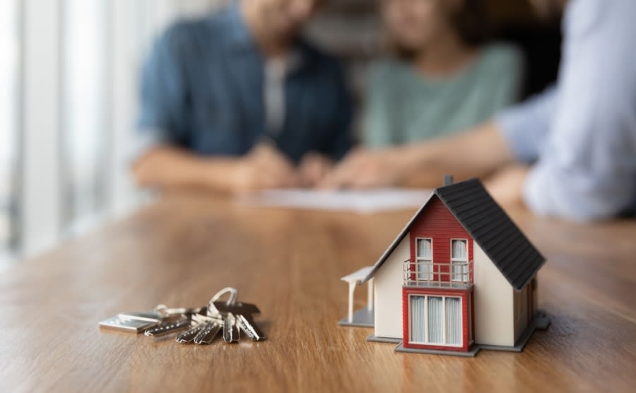Close up of key and tiny toy house on table. Married couple buying house, consulting, lawyer, legal advisor, real estate agent, bank manager, signing mortgage agreement in background
