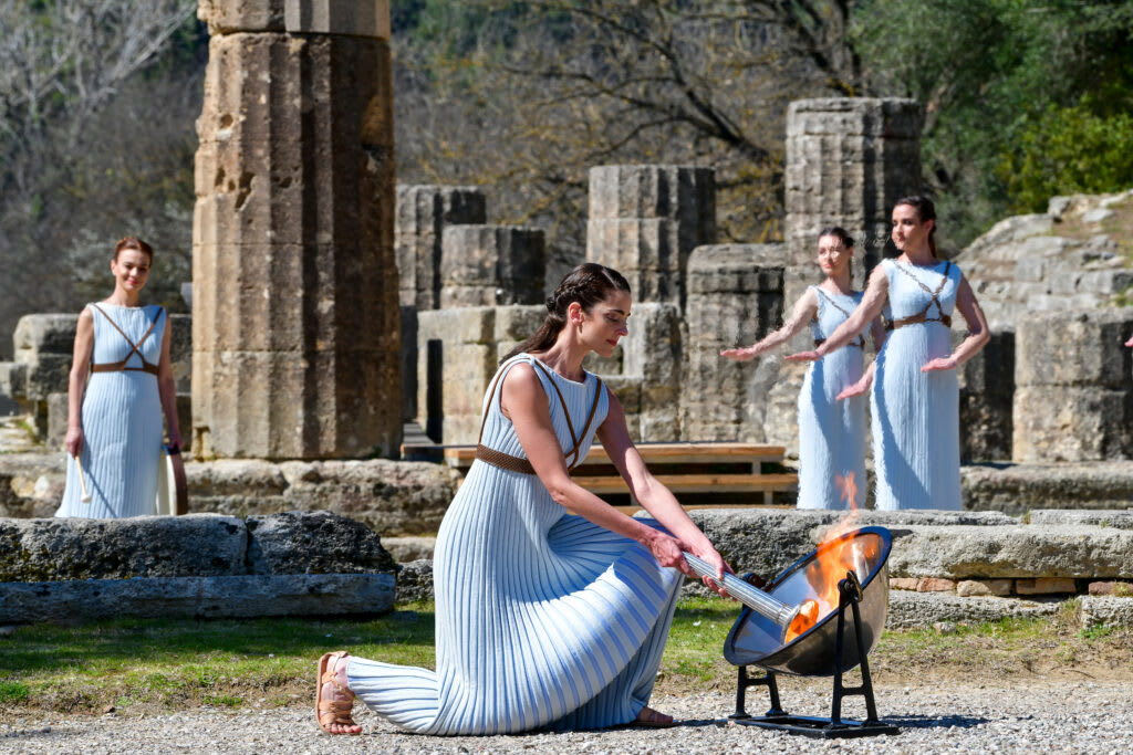 Women in ancient Greek costumes lighting the Olympic torch